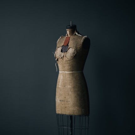 An antique dress form with patches and some areas more worn out than others stands tall in the ambient natural light. Used as reference for the handmade collection.